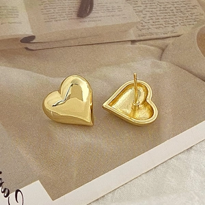 Macro detail of glossy gold heart-shaped stud earrings on a warm magazine background