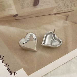 Detailed close-up of 3D heart-shaped silver earrings on soft beige fabric background