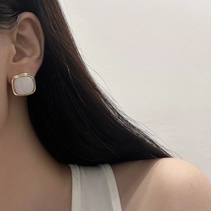 Close-up of geometric gold-edged earrings with white inlay worn by a model
