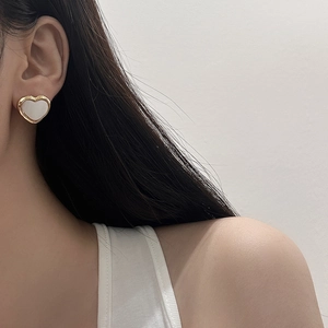 Close-up of elegant gold heart earrings with white mother of pearl inlay on model