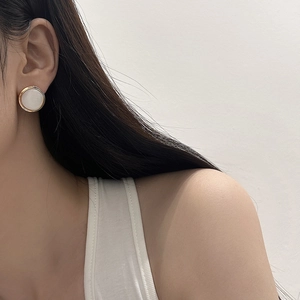 Detail showing elegant gold circular earrings with white pearlescent inlay on ear