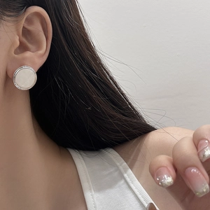 Close-up of geometric silver stud earring with white pearl-like inlay on model ear