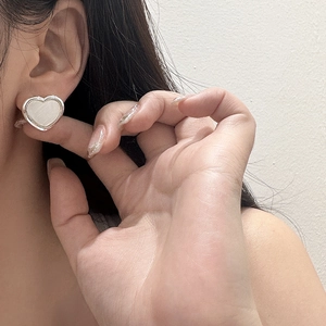 Close-up of a heart-shaped silver earring with a white shell inlay worn on a model's ear