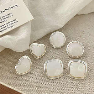 Detailed close-up of geometric silver earrings with white pearl inlay on fabric