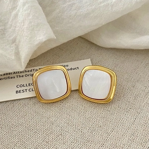 Detailed close-up of French geometric gold earrings with pearlescent resin inlay