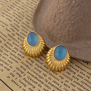 Gros plan de boucles d'oreilles dorées texturées avec des pierres œil de chat bleues