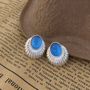 Détail de boucles d'oreilles vintage en argent avec pierre œil de chat bleue sur fond rétro