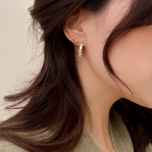 Détail de boucles d'oreilles dorées avec zircons et clou haltère portés à l'oreille