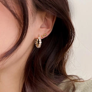 Gros plan d'une boucle d'oreille créole dorée avec diamants pavés et d'une puce sur un mannequin