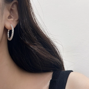 Détail de boucles d'oreilles créoles argentées pavées de pierres portées par un mannequin