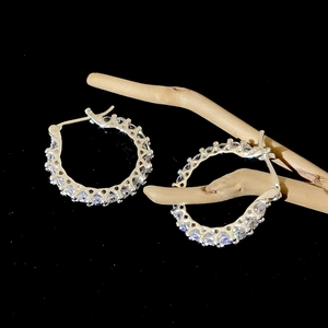 Détail de créoles argentées serties de strass brillants sur une branche en bois