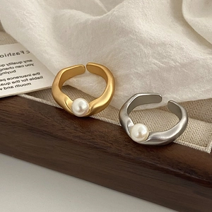 Anelli aperti opachi in oro e argento con perle bianche su sfondo di tessuto bianco