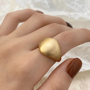 Detailed view of matte gold wide ring with irregular organic pebble design on finger