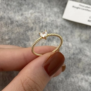 Dettaglio di un anello dorato con zircone a cuore e fascia a corda intrecciata