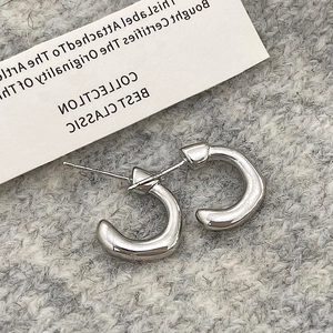 Gros plan de boucles d'oreilles créoles argentées en C sur un tissu en maille grise élégant