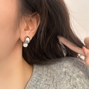Minimalist silver irregular droplet pearl earrings worn by a model on a grey sweater