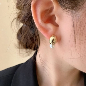 Close-up of a minimalist gold metal pebble and white pearl earring on a model ear