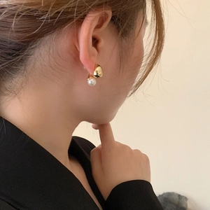 Detailed close-up of a minimalist gold bean and white pearl earring worn by a model