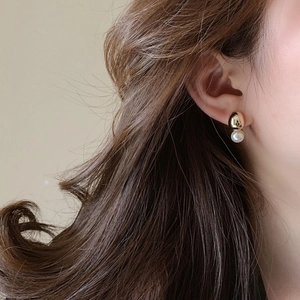 Close-up of minimalist gold bead and white pearl earrings worn on a female model