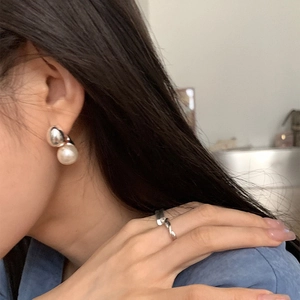 Detail of silver bead and white pearl earrings set with a twisted band ring on model