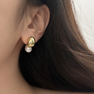 Detail of minimalist gold bead and white pearl earring worn on the earlobe