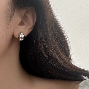 Close-up of a minimalist silver bean-shaped stud earring worn on a model's ear