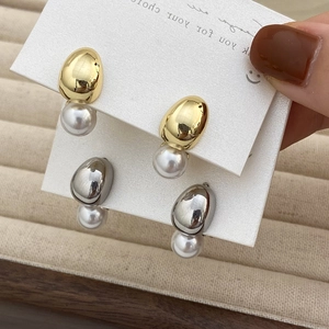 Close-up of minimalist gold and silver earrings featuring metal studs and round pearls