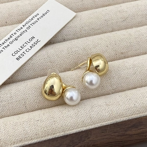Detailed macro view of gold ball and pearl earrings on a beige velvet jewelry display tray