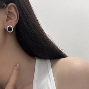 Close-up of minimalist silver oval earrings with black stone inlay worn by a model