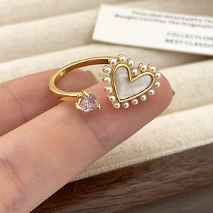 Detail van gouden open ring met parelmoeren hart en roze hartvormige zirkonia steen