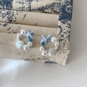 Dettaglio macro di orecchini a stella marina e perle con strass blu e smalto colorato