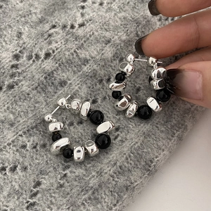 Detail of silver irregular metal beads and polished black stones on elegant hoop earrings