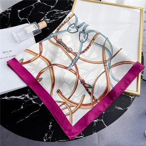 Close-up of silk-textured square scarf with horse harness patterns on a gold frame