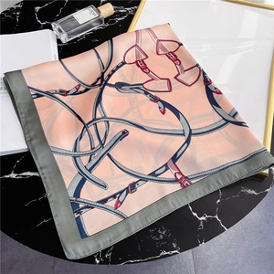 Detail of silk square scarf with belt buckle print and gray border on marble surface