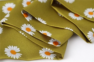 Detailed view of green silk-like scarf featuring white daisy prints and woven texture