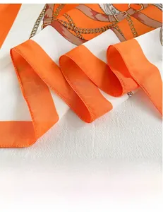 Detail of silk scarf showing orange color block with golden chain and horse buckle print
