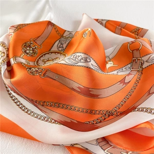 Close-up of orange and beige silk scarf with elegant chain and buckle patterns