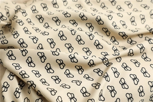 Detailed view of beige silk scarf with elegant black butterfly prints and soft texture