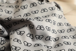 Detail of soft silk square scarf showing elegant black butterfly patterns on silver fabric
