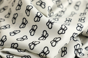 Macro shot of silk scarf fabric showing elegant black butterfly patterns on white satin