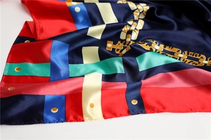 Détail de la texture du foulard en soie avec rayures géométriques et motifs chaînes dorées
