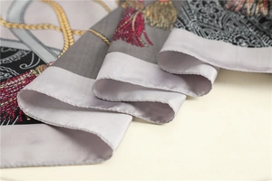 Détail d'un foulard en soie montrant glands rouges, chaînes dorées et motifs paisley sur gris