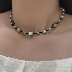 Macro detail of cat head shell pendant and gray pearl necklace worn on model neck