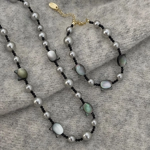 Gray pearl necklace with black cat-shaped shell pendant on a cozy knit fabric background