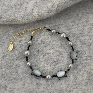 Detailed shot of cat shell beads and grey pearls on a handcrafted bracelet with gold clasp