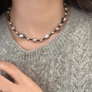 Elegant pearl necklace with black beads and a cat shell pendant worn on grey knitwear