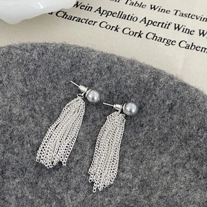 Macro shot of long silver tassel earrings with grey round pearls on a textured background