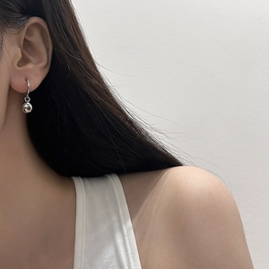 Close-up of minimalist silver hoop earrings with polished ball pendants on model