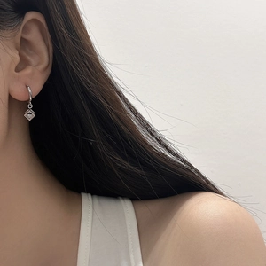 Close-up of a silver earring with a sparkling square zircon on a model's ear