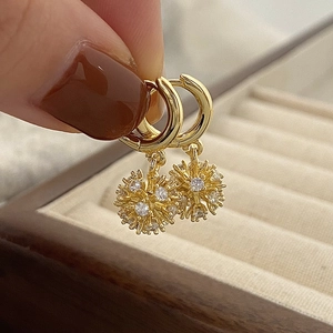 Detail of gold starburst earrings with sparkling zircon crystals held over a jewelry box